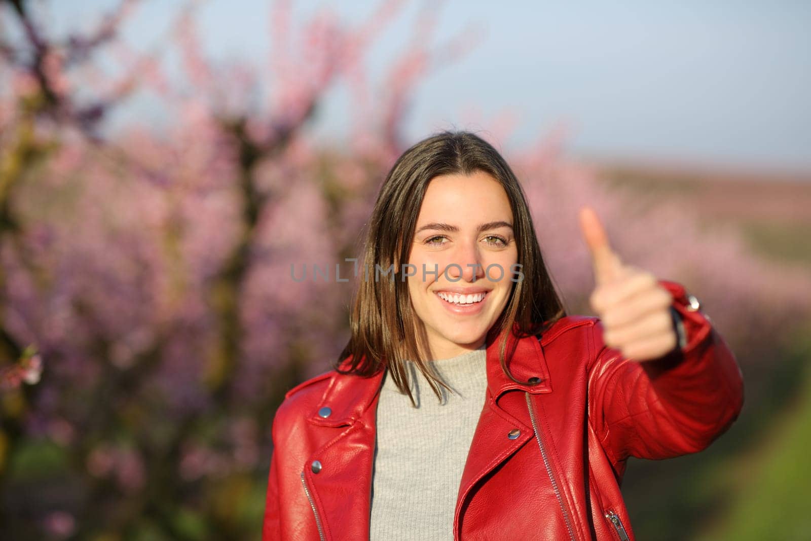 Happy woman in red gesturing thumb up in a field