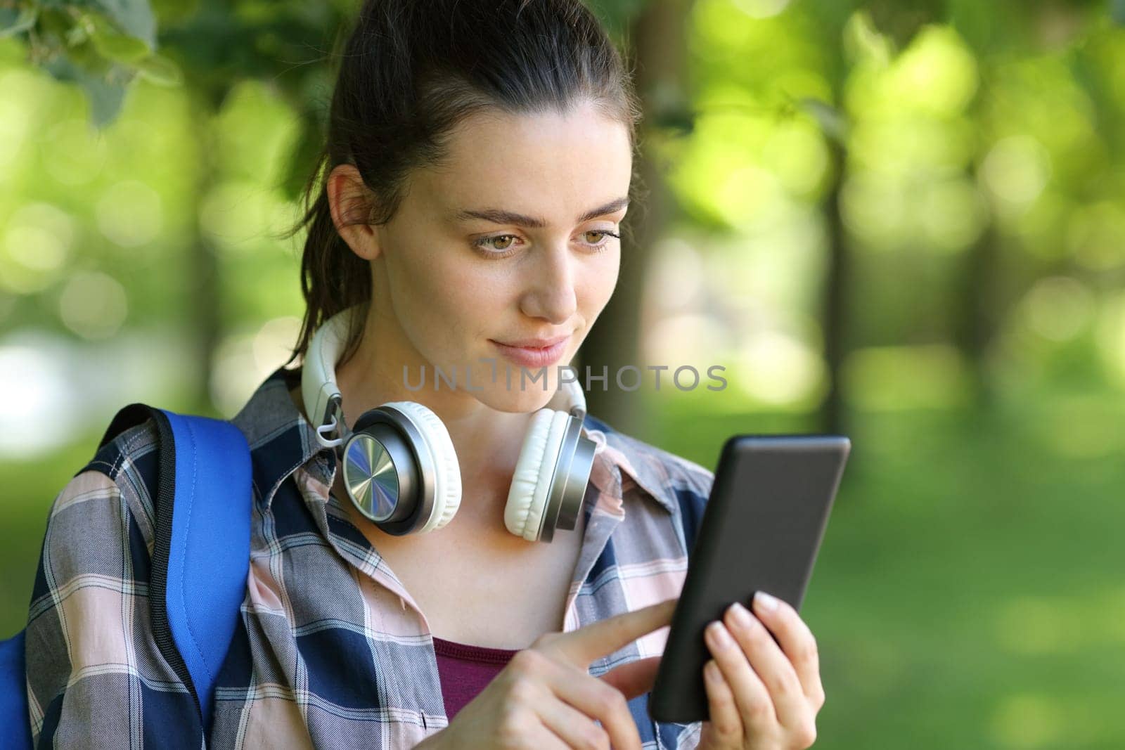 Student checking phone walking in a green park or campus