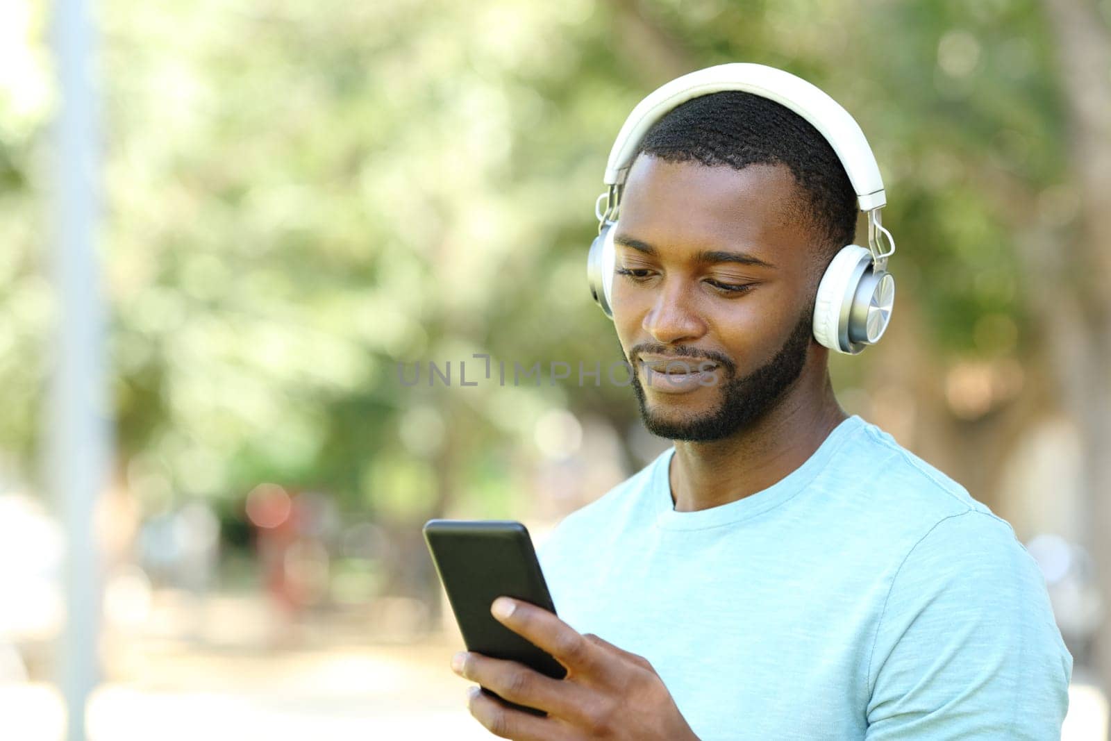Man with black skin listening to music with phone in park