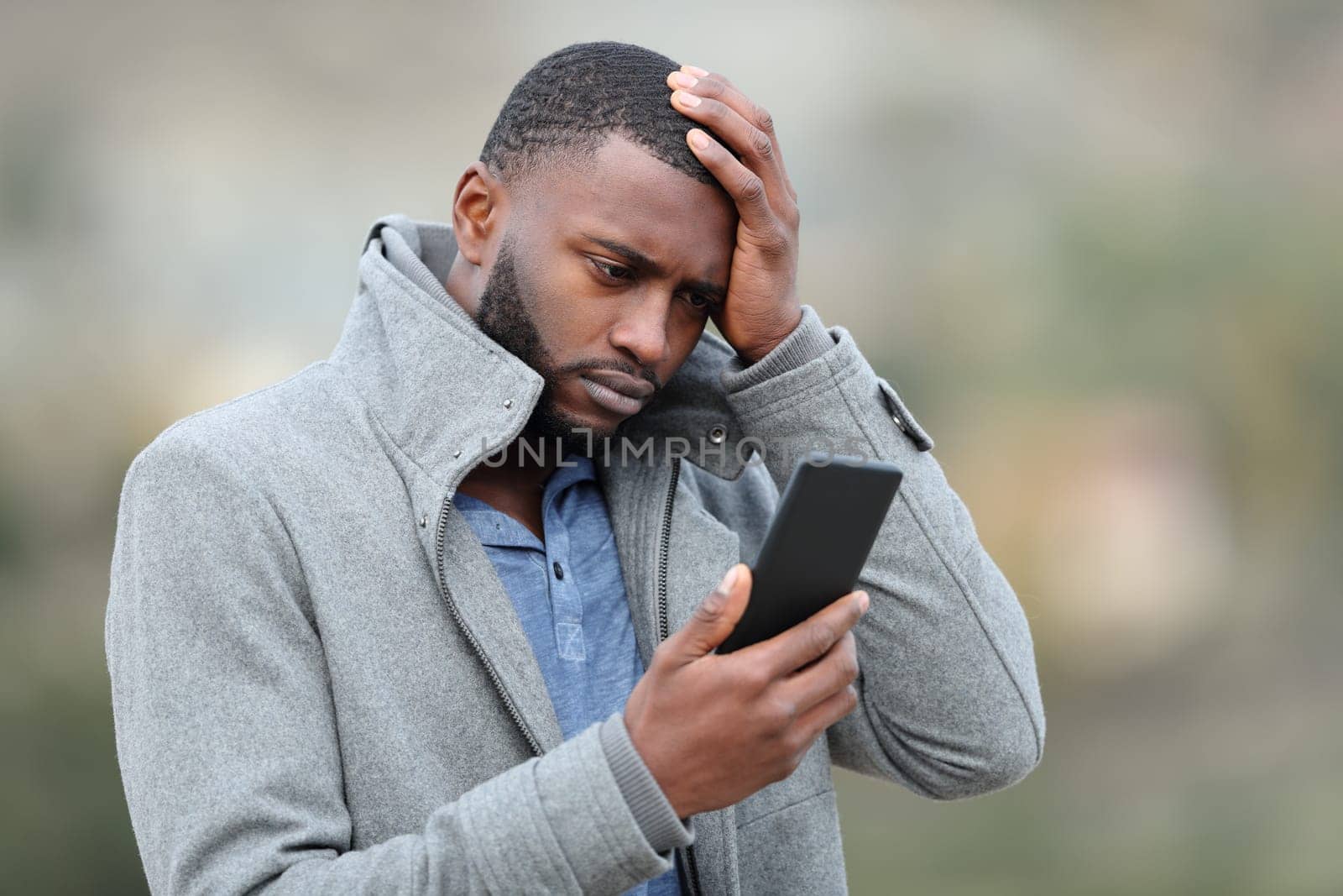 Worried man with black skin checking phone in winter