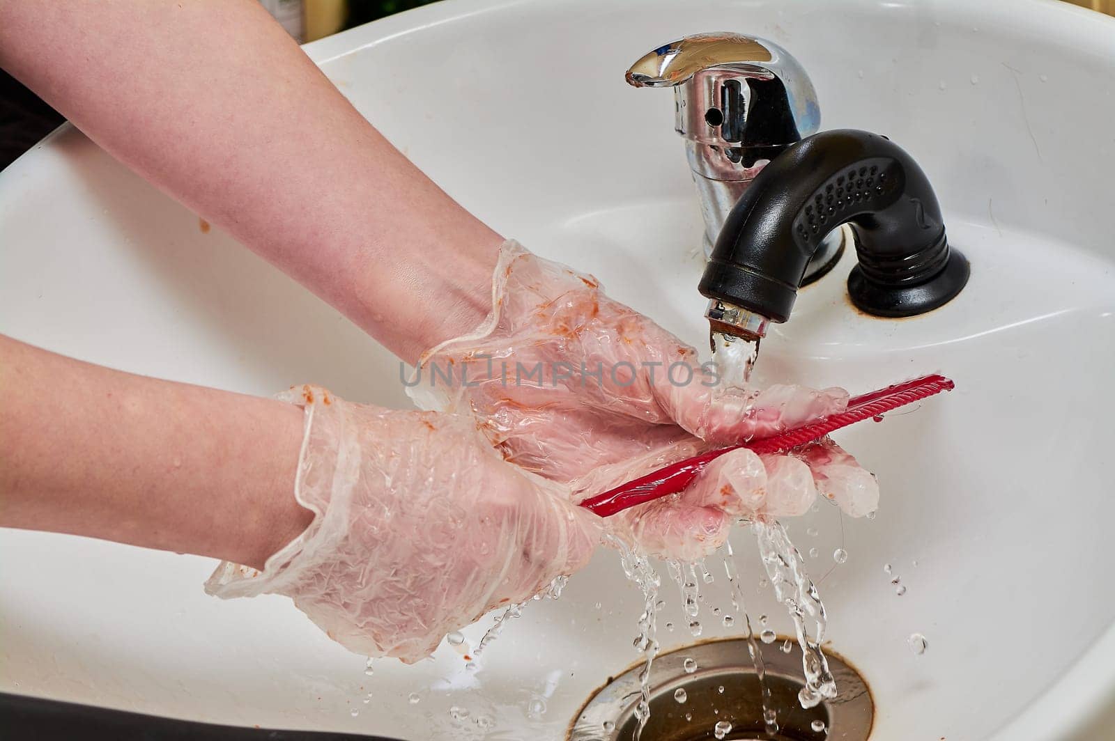 Women's hands in hair coloring gloves wash a comb under a stream of water in a white sink. High quality photo