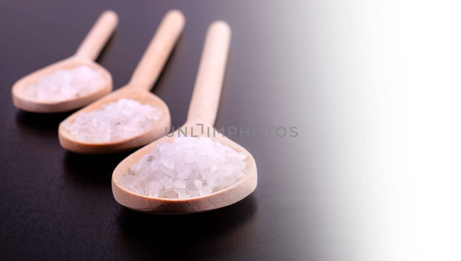 The Bath salt in three wooden spoons on a dark polished desk in backlight