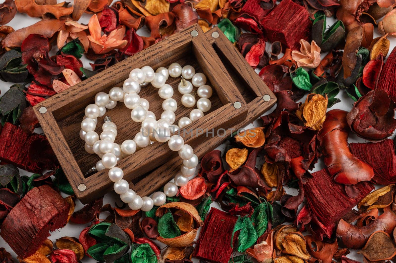 Pearl jewelry in wooden box on dry flowers background.