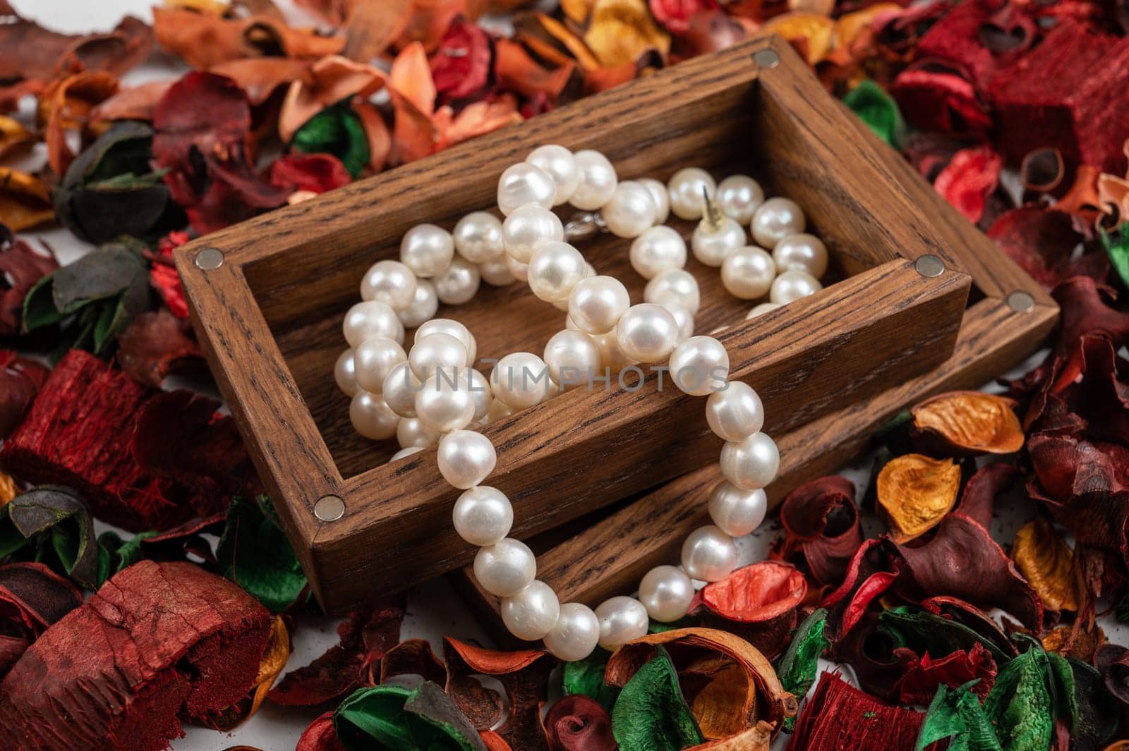 Pearl jewelry in wooden box on dry flowers background.