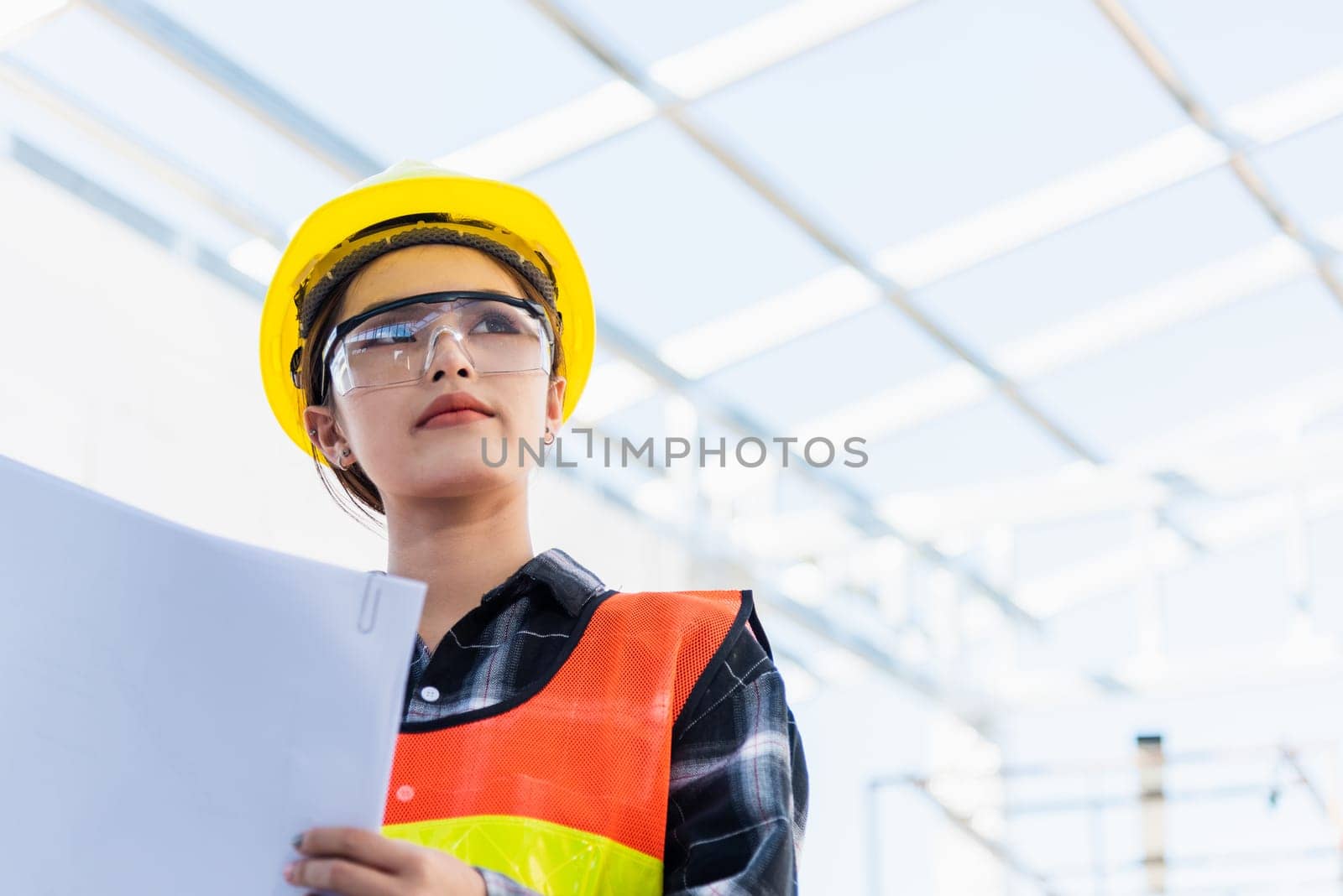 Asian engineer architect worker woman holding blueprint infrastructure progress at construction site, engineering female leader standing hold paper plan control worker to building project