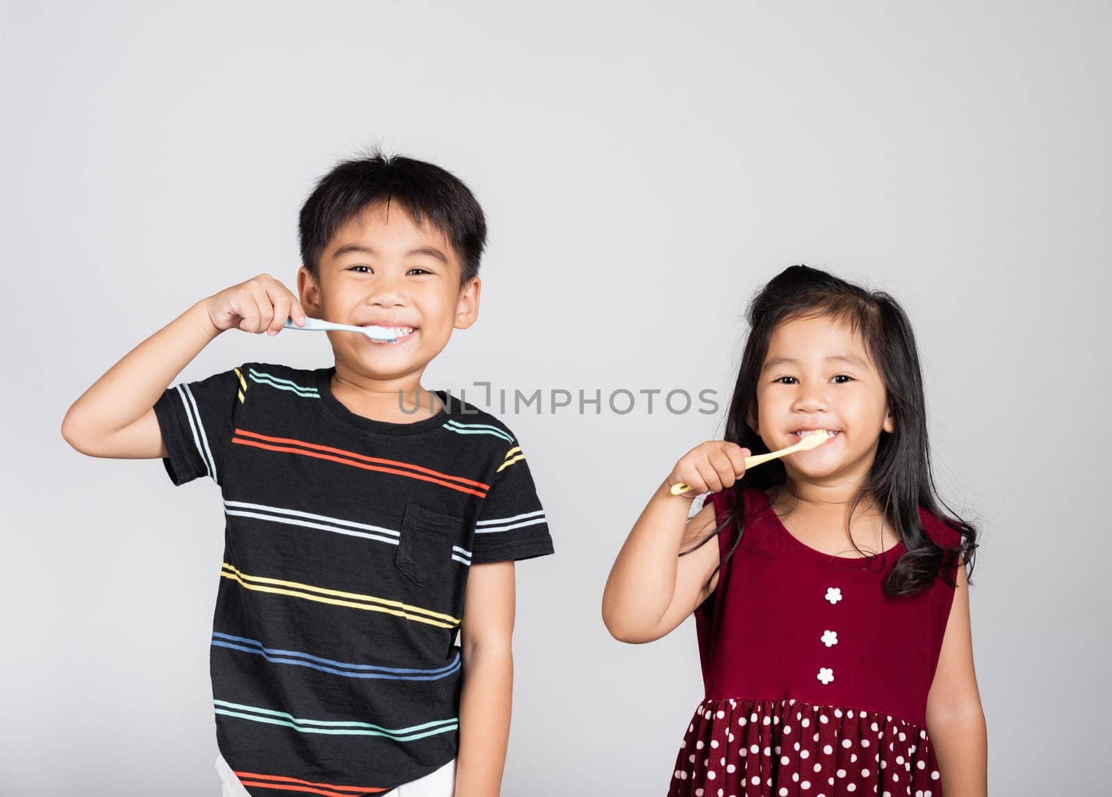 Little cute kid boy and girl 3-6 years old brushing teeth and smile in studio shot isolated on white background, happy Asian children holding toothbrush in mouth by himself, Dental hygiene healthy
