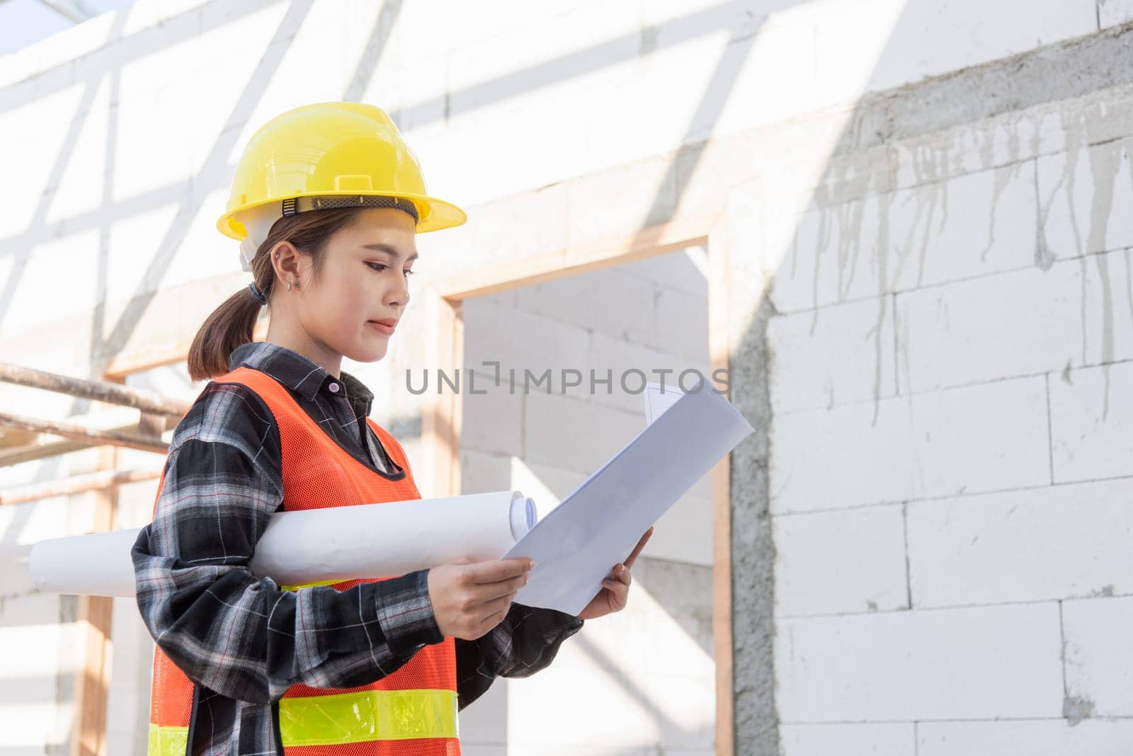 Asian engineer architect worker woman holding blueprint infrastructure progress at construction site, engineering female leader standing hold paper plan control worker to building project