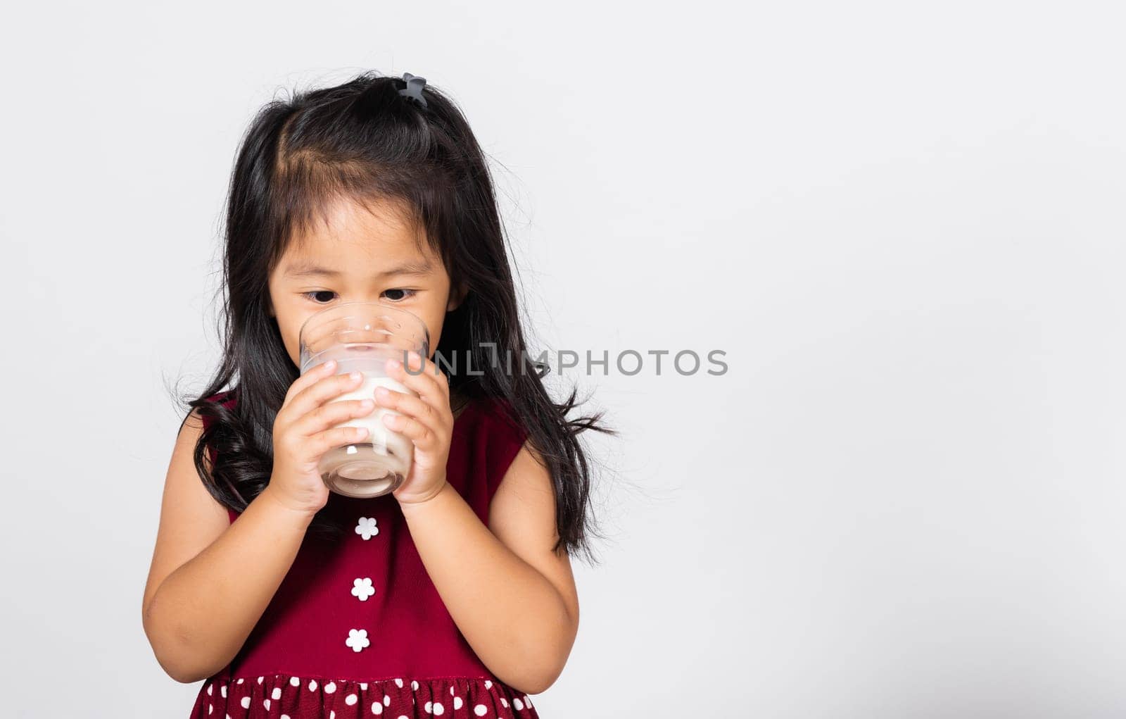 Little cute kid girl 3-4 years old smile holding milk glass he drinking white milk in studio shot isolated on white background, Asian children preschool, Daily life health care Medicine food