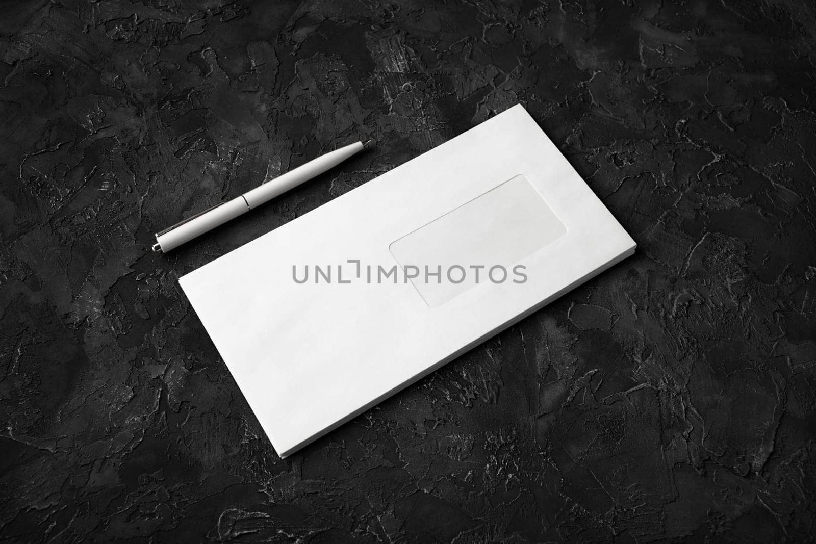 Blank envelope and pen on black stone background.