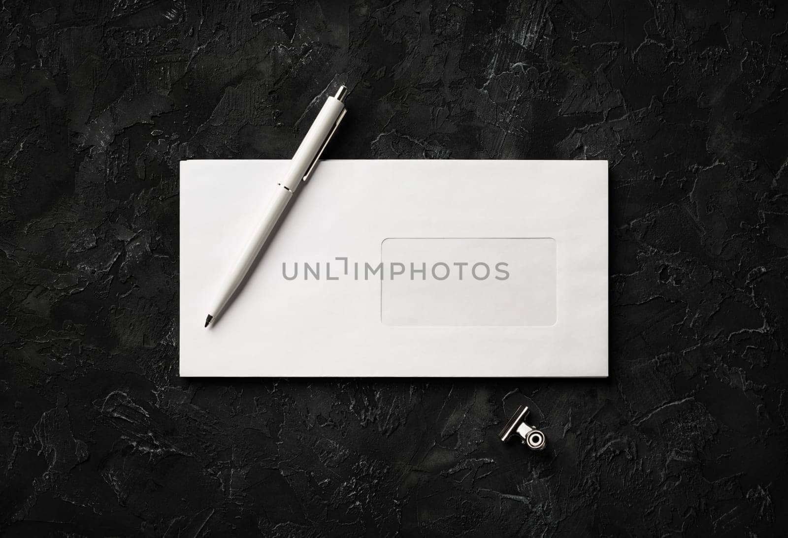 Blank envelope, pen and clip on black stone background. Branding mock up. Flat lay.