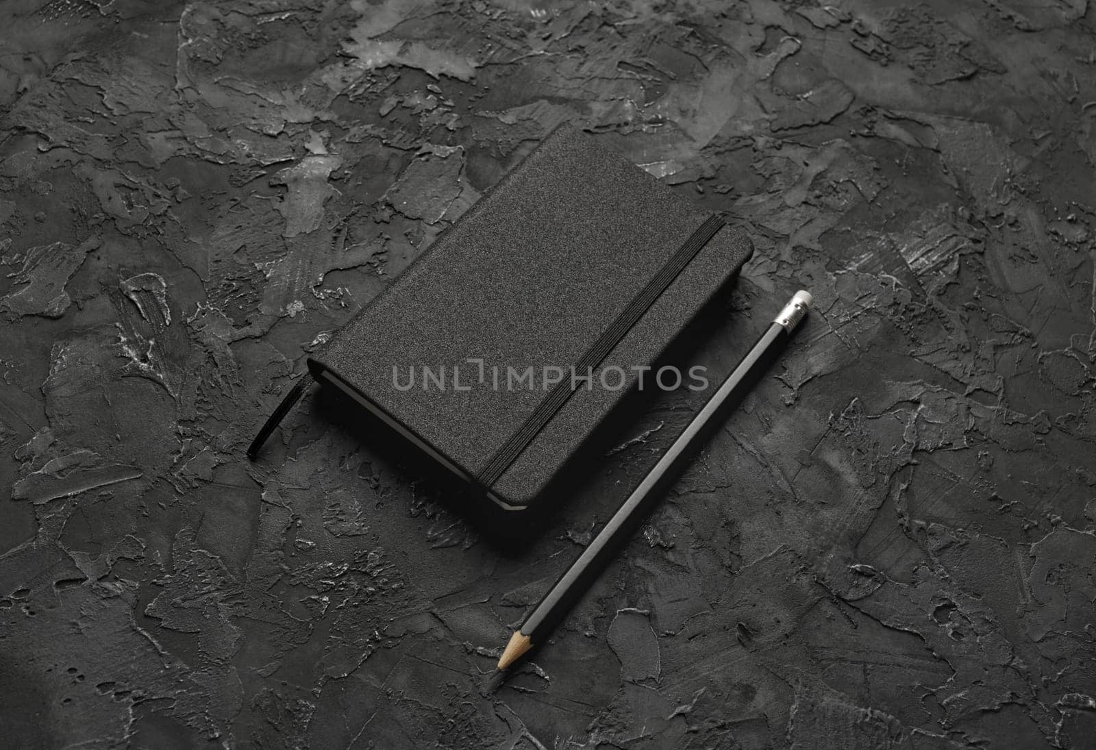 Blank black notebook and pencil on black stone background.