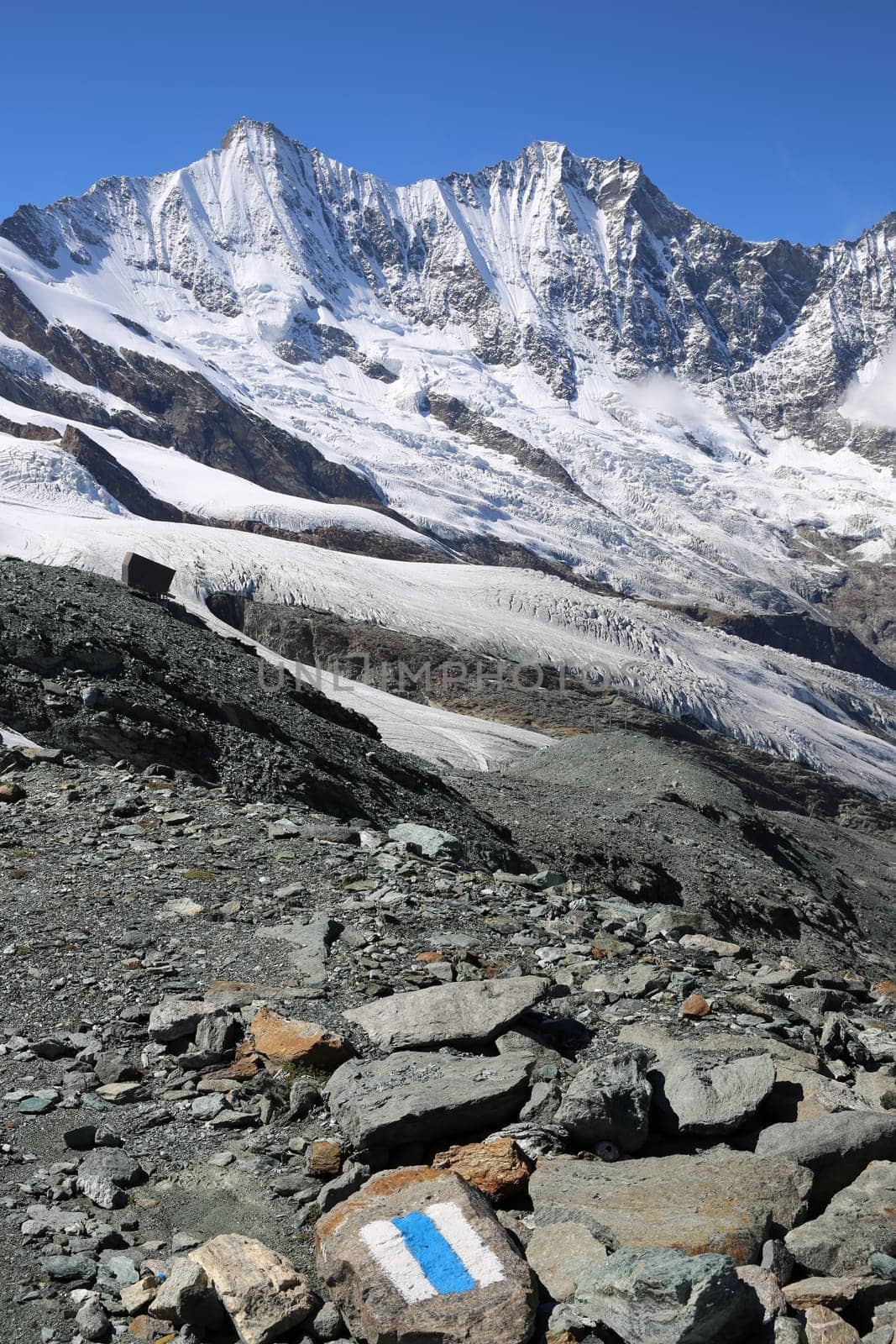 White and blue trail sign painted on a Rock. Saas-Fee. Swiss Alps