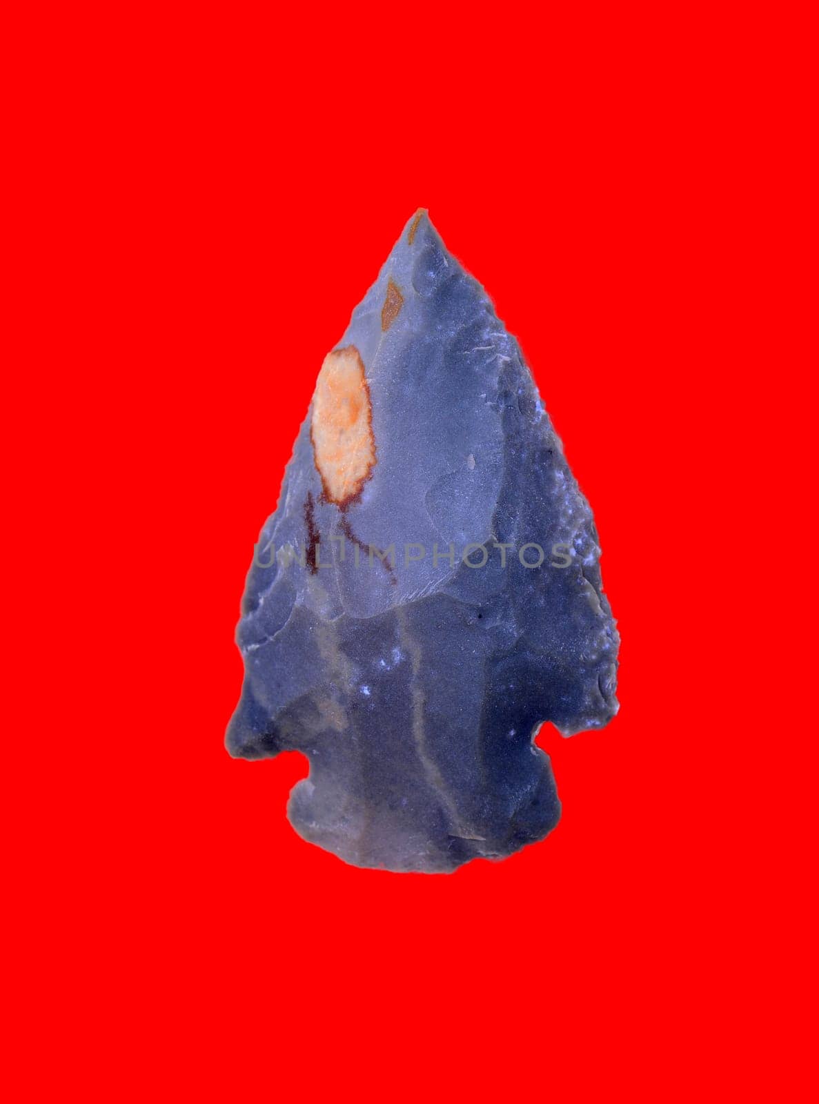 Ancient Prehistoric primitive stone arrowhead isolated over red