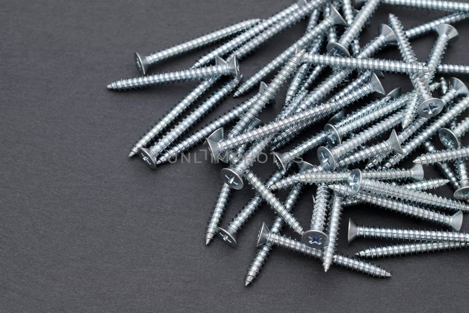 Pile of silver metallic tapping screws on black background
