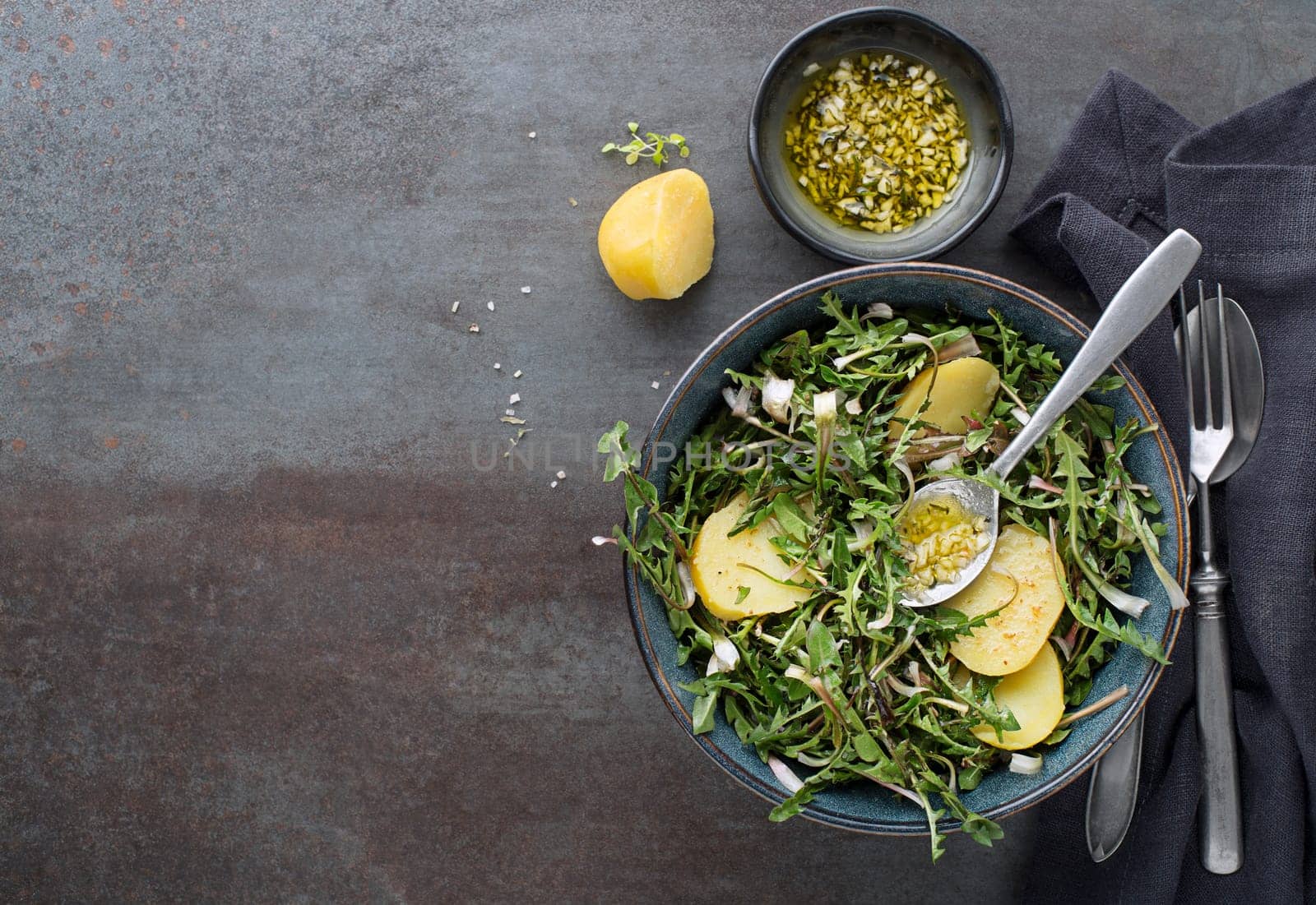 Healthy dandelion salad with potatoes and dressing on grey background close up