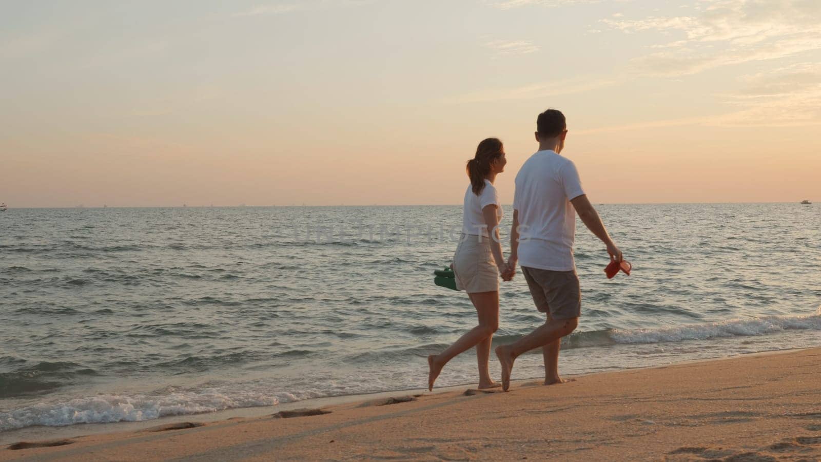 Vacation loving couple walking on beach together at sunset landscape, relaxing vacation travel summer, Asian man and woman in love holding hands walks along the sandy seashore