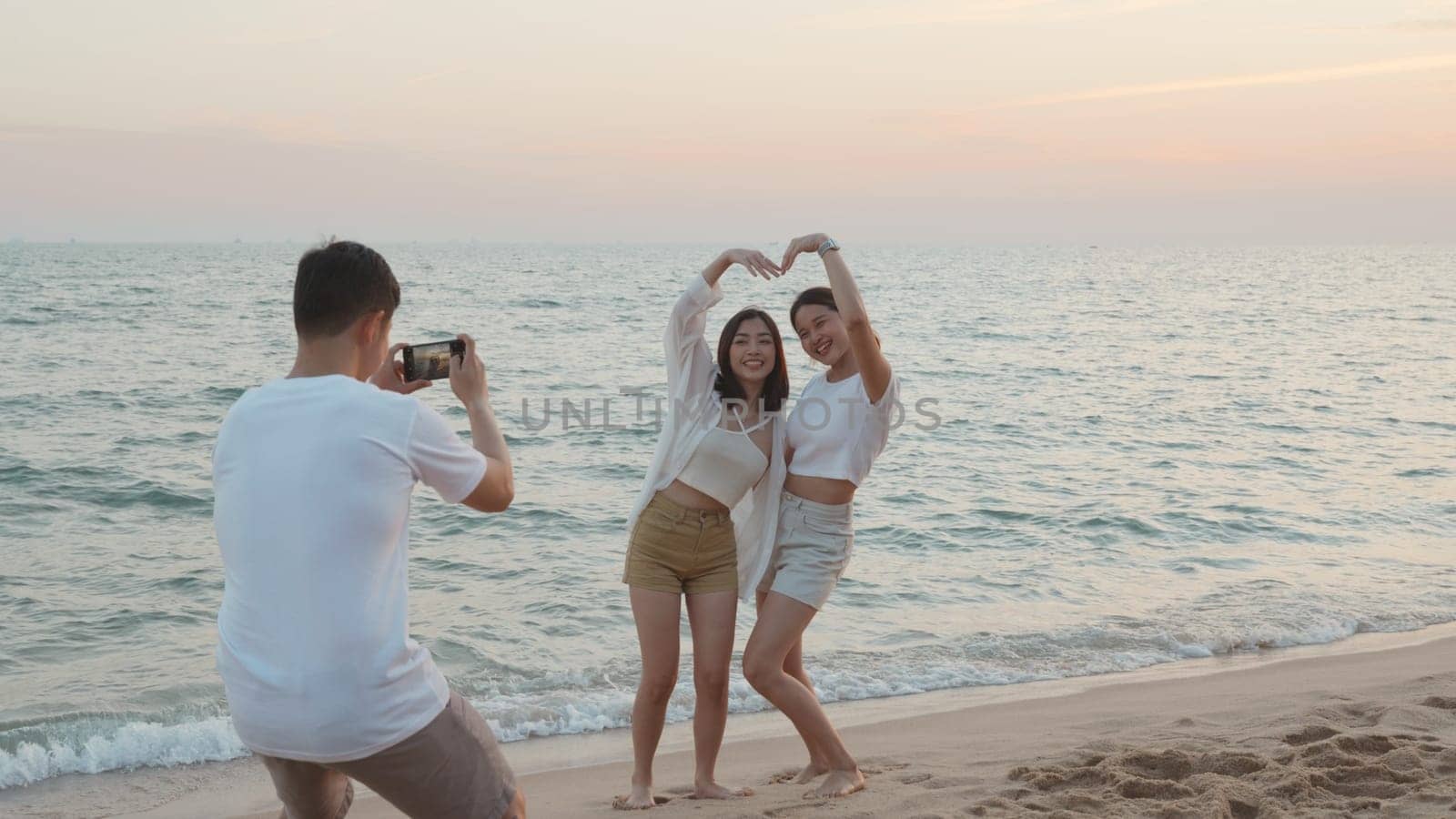 Happy friends smiling and posing taking photo from smartphone and having fun together on beach in holiday vacation time at sunset, Young Asian group woman and man in summer travel outdoor