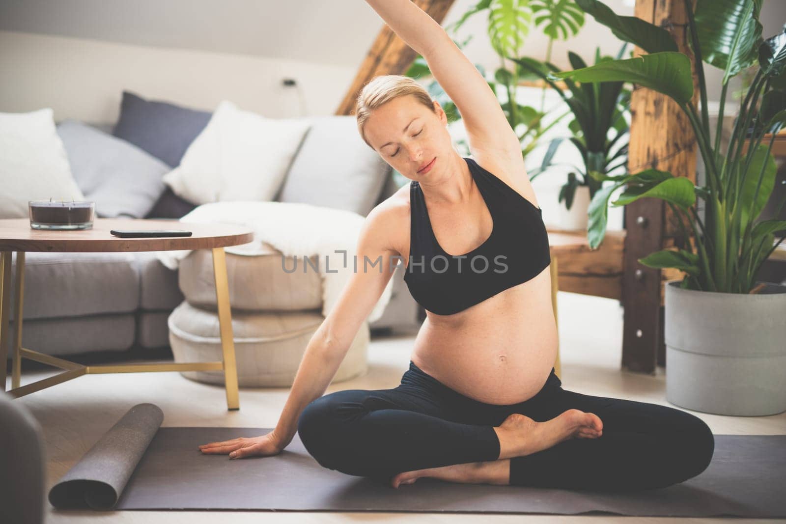 Young beautiful pregnant woman training yoga at home in her living room. Motherhood, pregnancy, healthy lifestyle and yoga concept.
