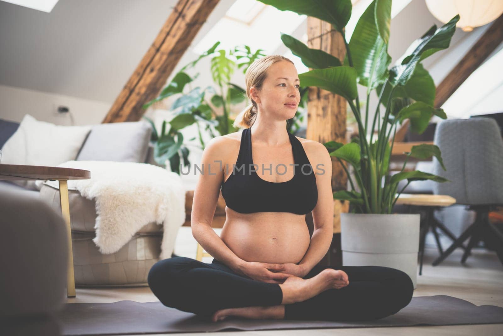 Young beautiful pregnant woman training yoga, caressing her belly. Young happy expectant relaxing, thinking about her baby and enjoying her future life. Motherhood, pregnancy, yoga concept
