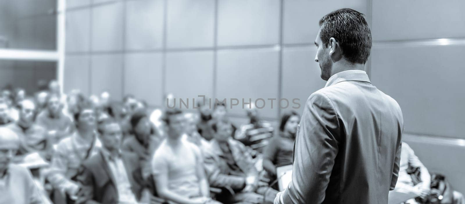 Speaker giving a talk on corporate business conference. Unrecognizable people in audience at conference hall. Business and Entrepreneurship event.