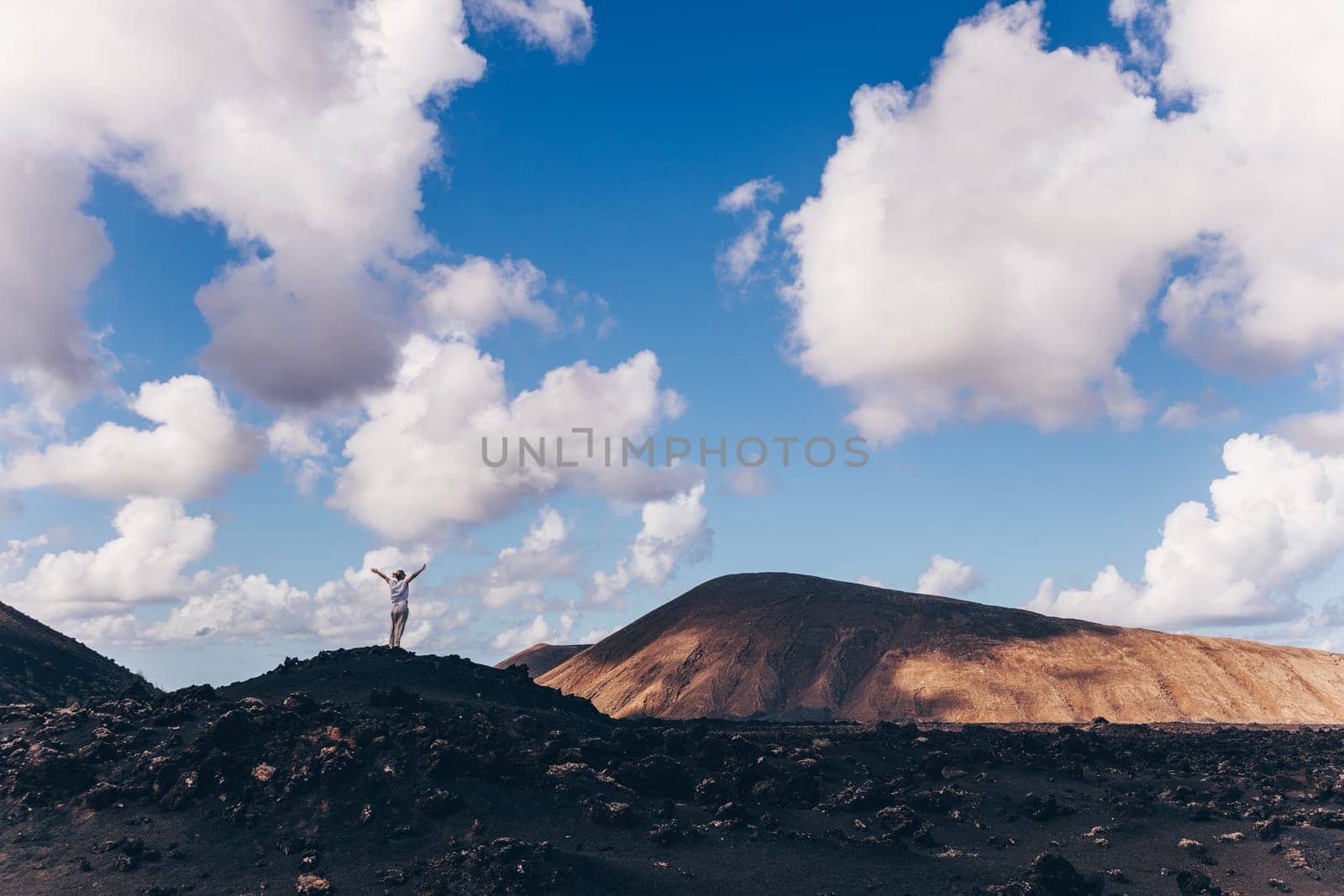 Woman rising hands up in the sky, enjoying amazing views of volcanic landscape in Timanfaya national park on Lanzarote, Spain. Freedom and travel adventure concept
