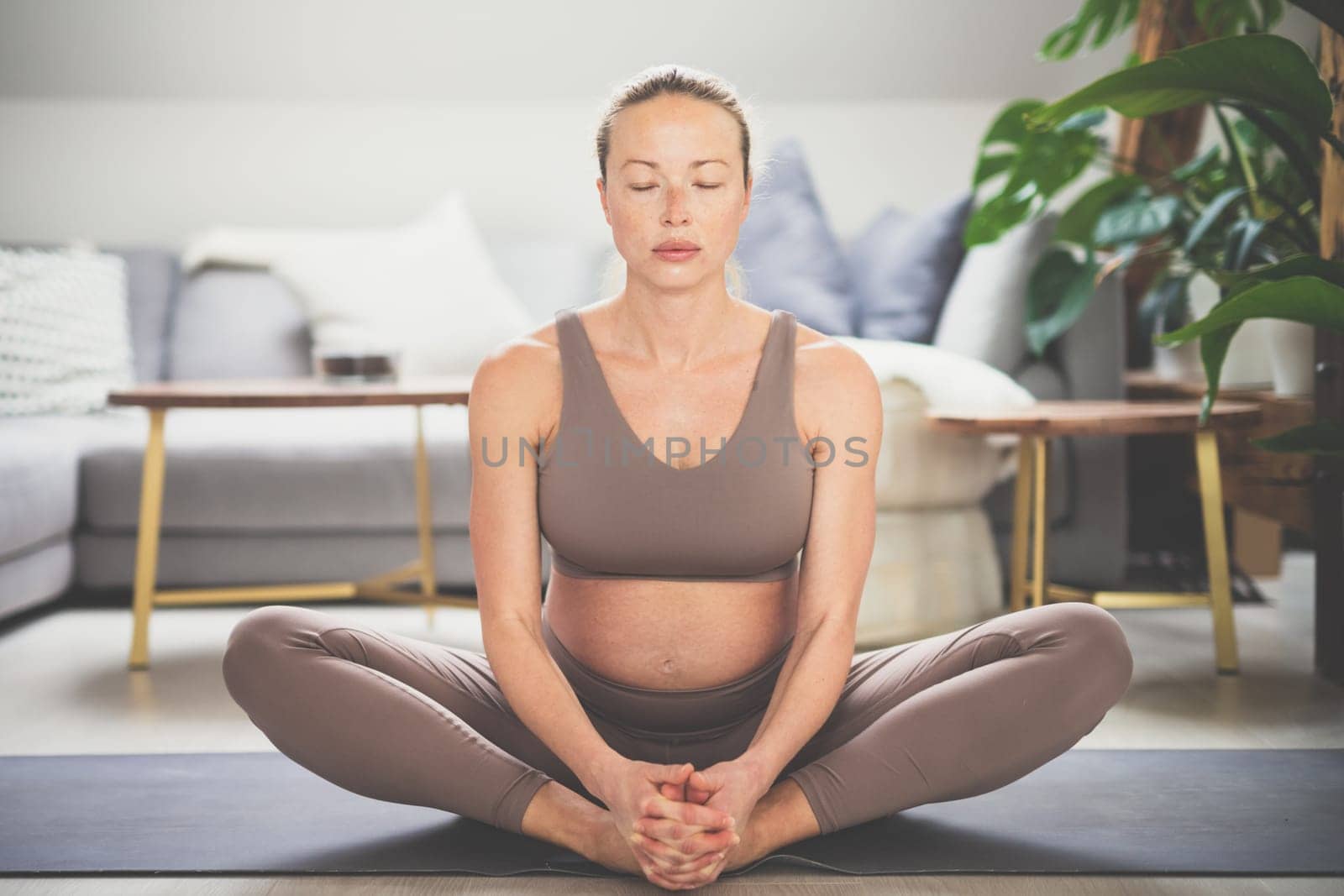 Young beautiful pregnant woman practising yoga at home in her living room. Motherhood, pregnancy, healthy lifestyle, well being and yoga concept