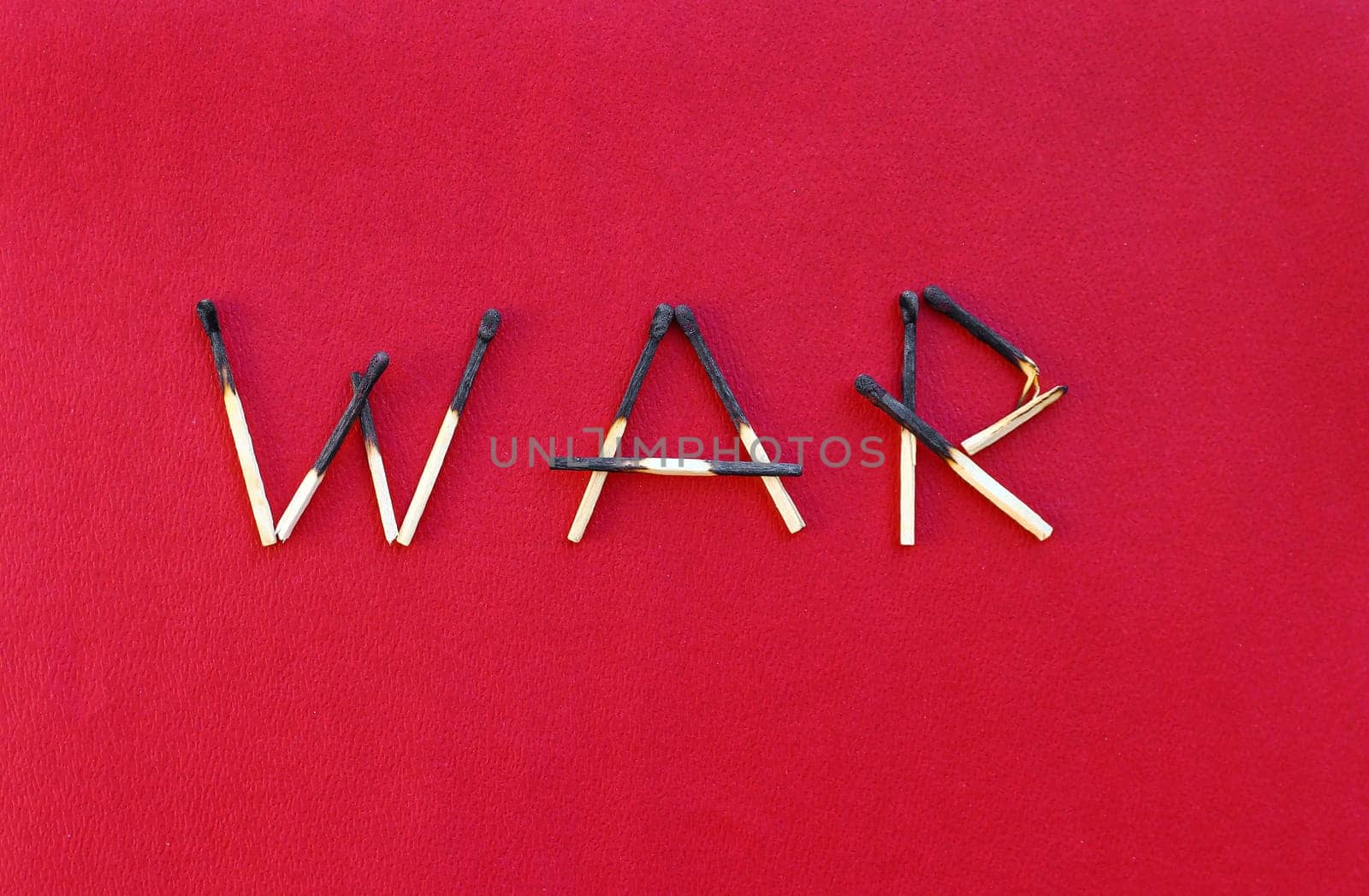 Burnt matches forming the word WAR on a red paper background