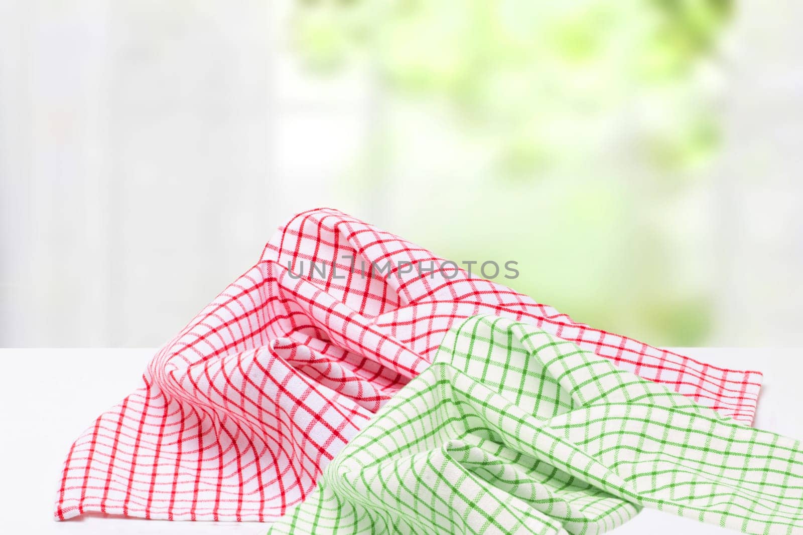 Empty desk table with red and green checkered tablecloth over abstract bright light green yellow spring or summer background. Template for your food and product display montage.