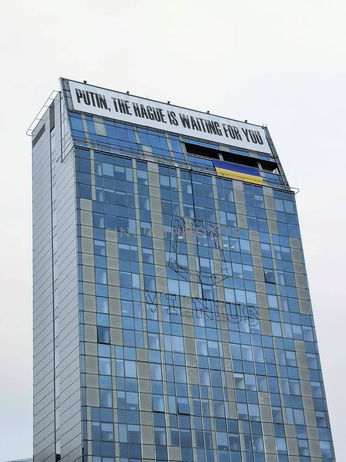 Vilnius, Lithuania: - 2022.03.07: Putin, The Hague is waiting for you inscription on the building of the Vilnius City Hall and the Ukrainian flag. THE UN Court in The Hague began consideration of the claim of Ukraine against Russia.