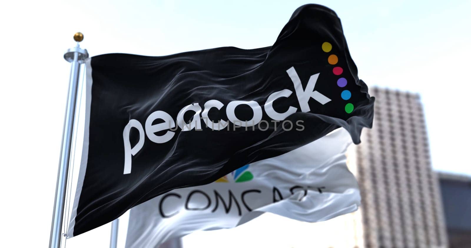 New York, USA, January 2022: Flag of Peacock TV waving in the wind with the Comcast flag in the background. Peacock is an American video streaming service owned by NBCUniversal