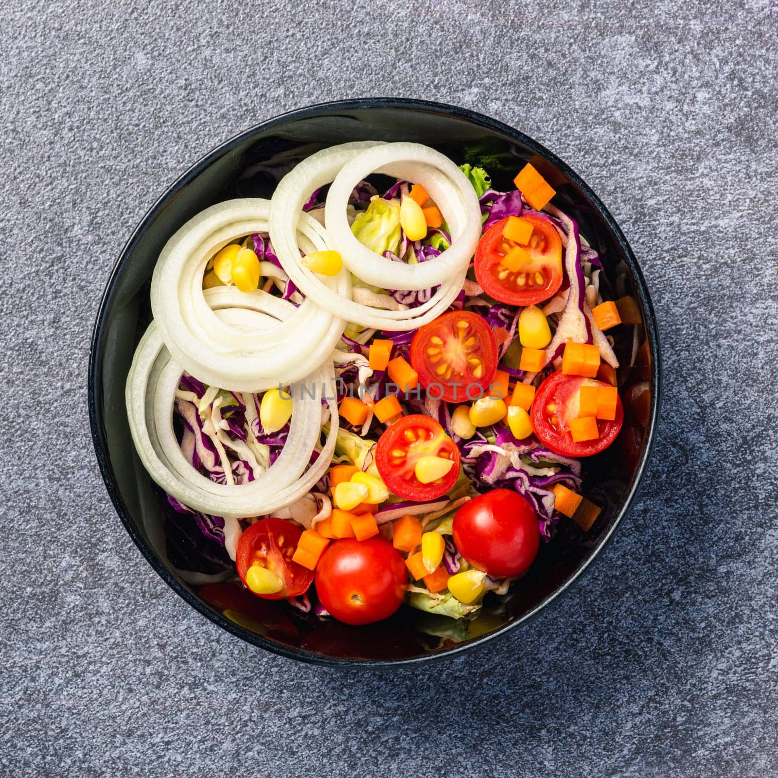 Top view of the healthy colorful salad bowl with tomatoes fresh mixed leaves vegetable in a dish on cement stone table background, Health salad snack diet food weight loss concept