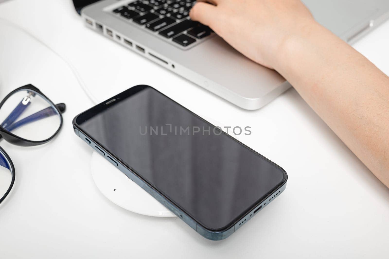 Charging smartphone battery with wireless charger device near laptop computer, Modern technology transfer energy mobile phone on workspace desktop at home office