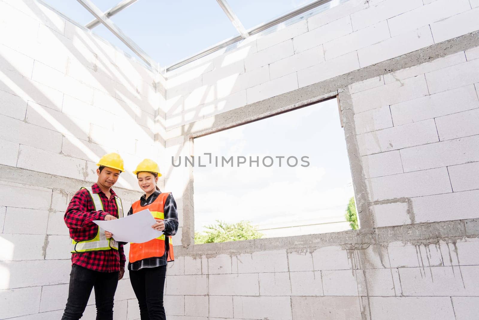Architect and client discussing the plan with blueprint of the building at construction site. Asian engineer foreman worker man and woman working talking and checking on draw paper to checking project