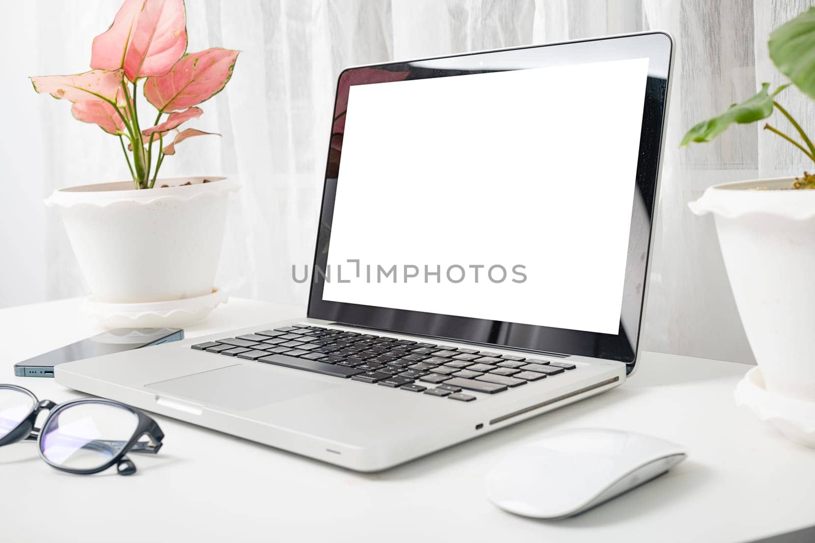 Modern workspace, mock up laptop computer blank white screen, eyeglasses and smartphone white table have potted plants on the desk, Notebook and mobile phone on desktop home office