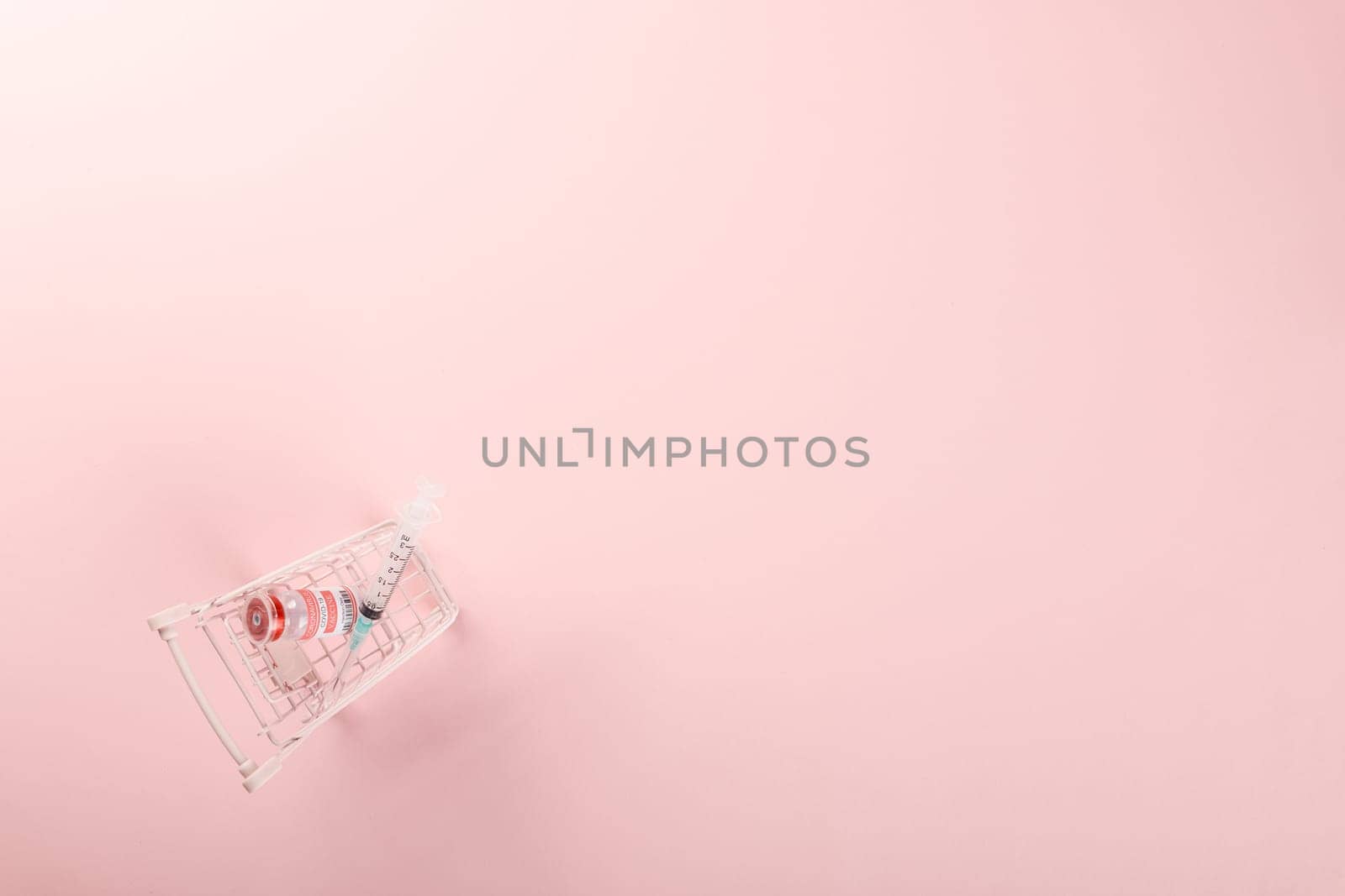 Shopping cart with vaccine vials bottles and syringes for vaccination against coronavirus, medicine illness, COVID-19 disease vaccine isolated on pink background
