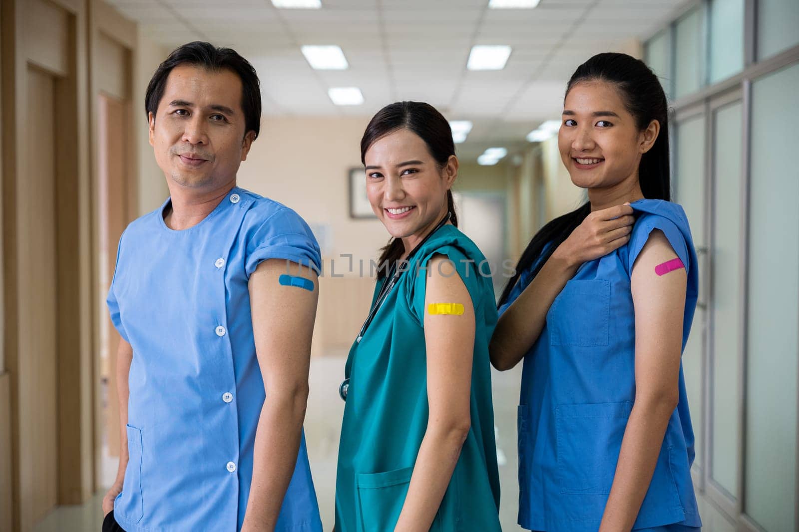 Medical personnel showing to bandage with plaster on arm after getting against Covid-19 vaccine, happy nurse woman and man standing at hospital, Covid-19 vaccination concept
