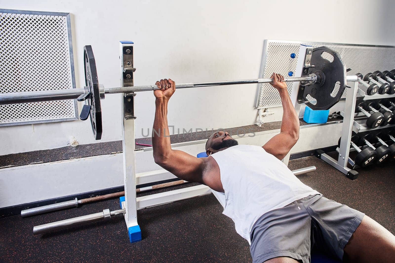 An African American man does a bench press lying on a bench in the gym. High quality photo