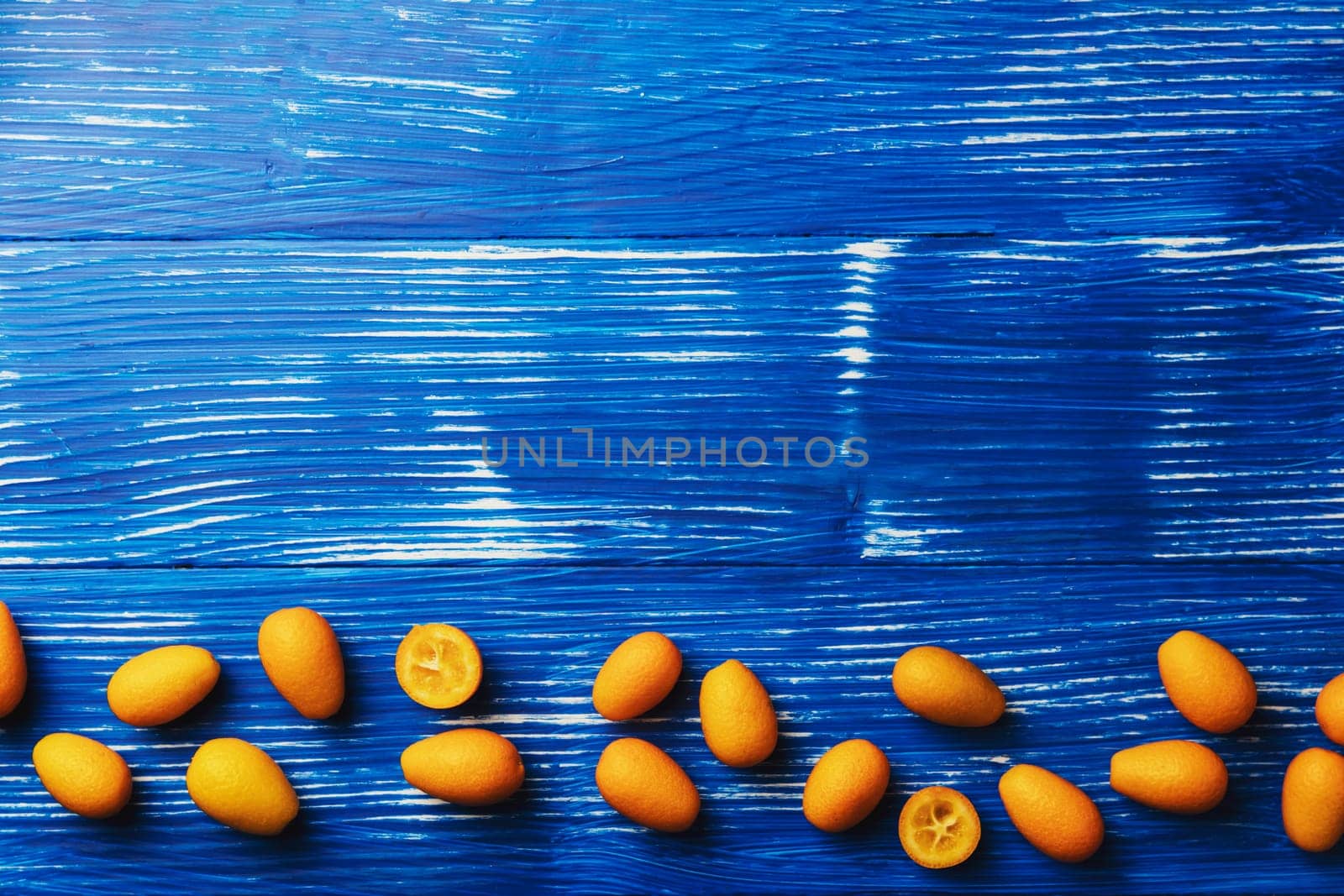 Light blue wooden flat lay table with top view on fresh ripe orange cumquat or kumquat citrus. Full, cut and sliced fruits. Empty copy space for advertisement text. High quality photo