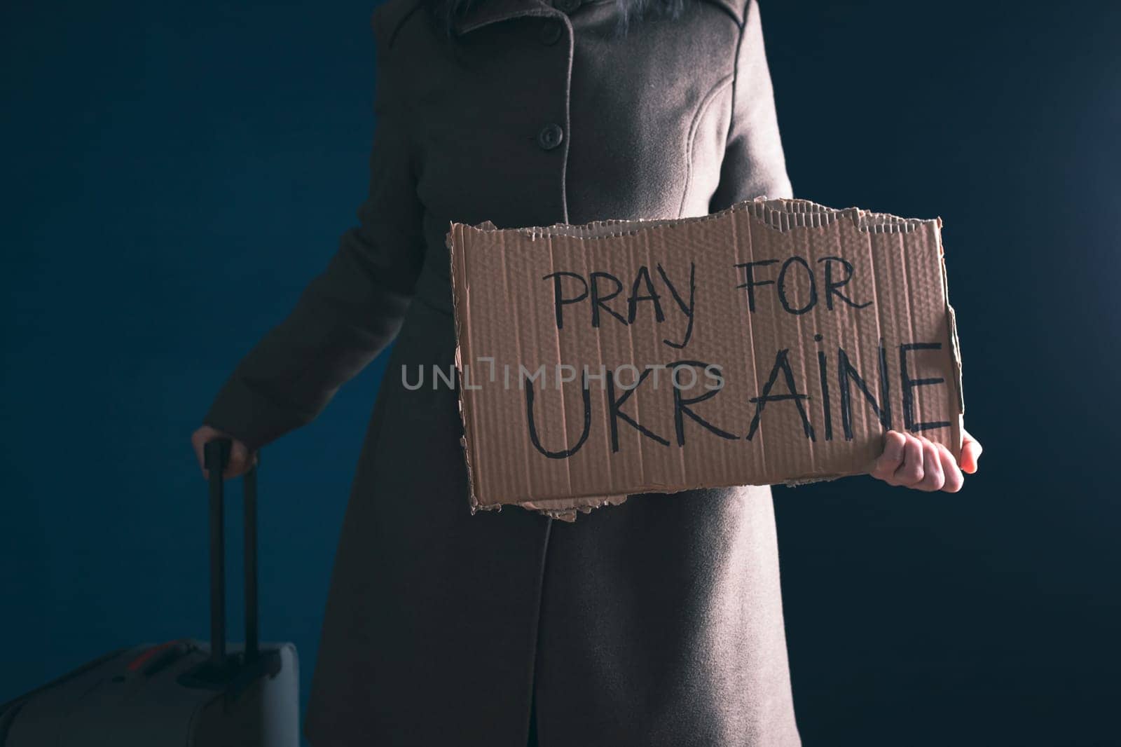 Ukrainian refugee holding placard with Pray for Ukraine text. Evacuation of civilians. Freedom to Ukraine concept.