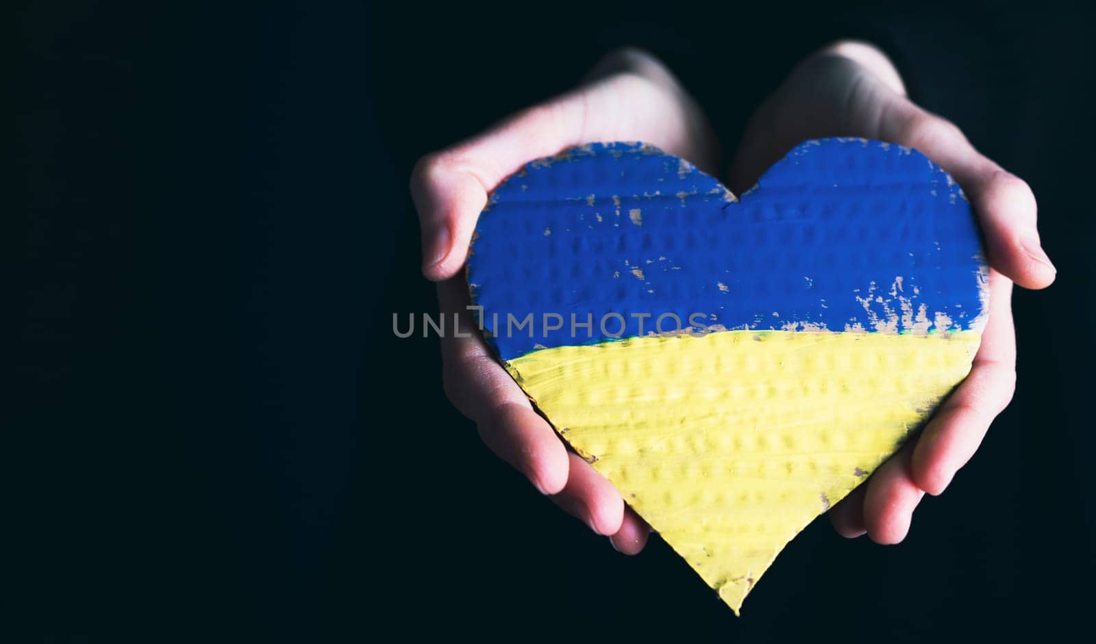 Heart shaped flag of Ukraine in female hands with copy space. The concept of solidarity with the citizens of Ukraine.