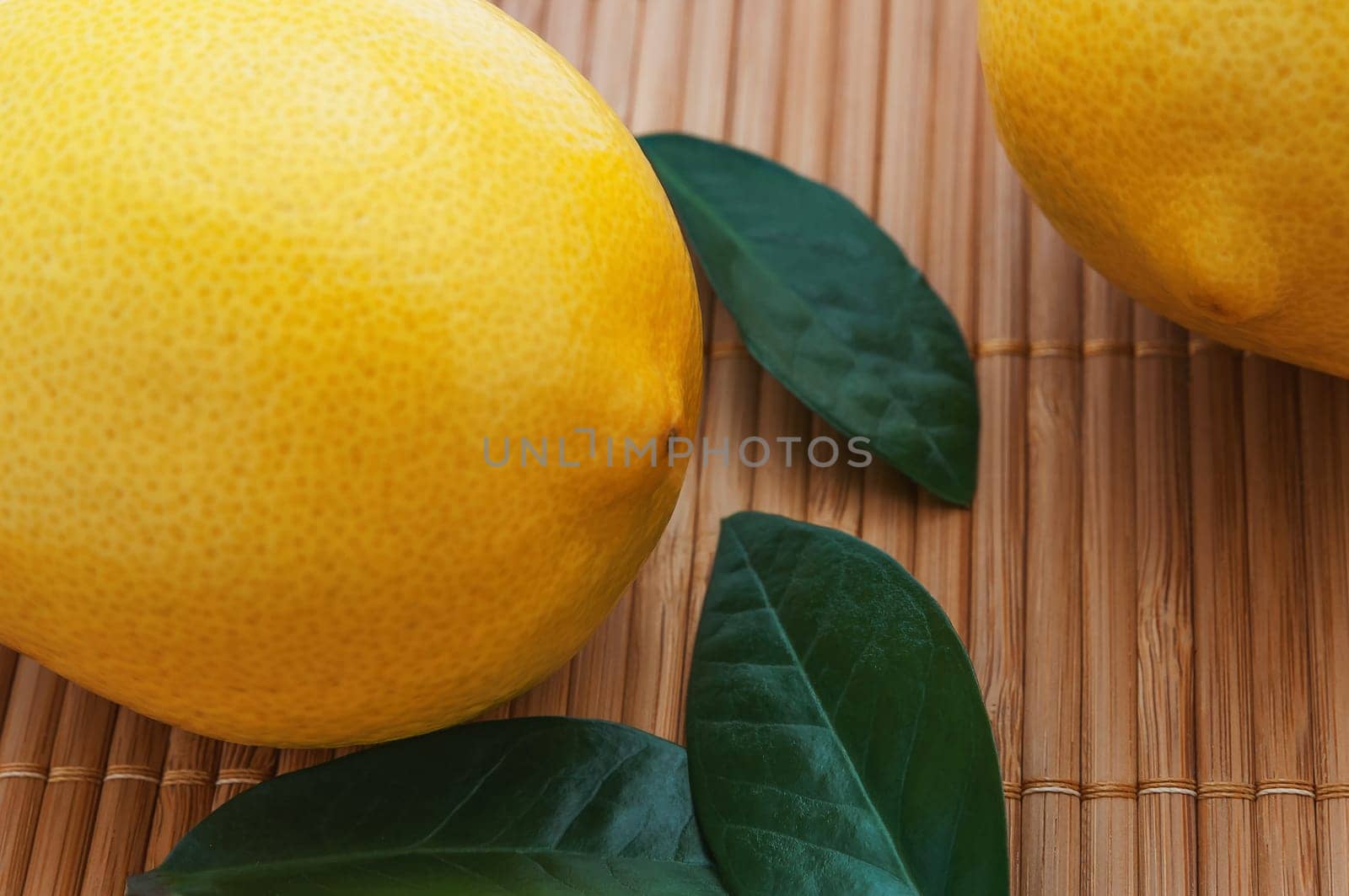 Close-up of large lemons and green leaves on bamboo mat.