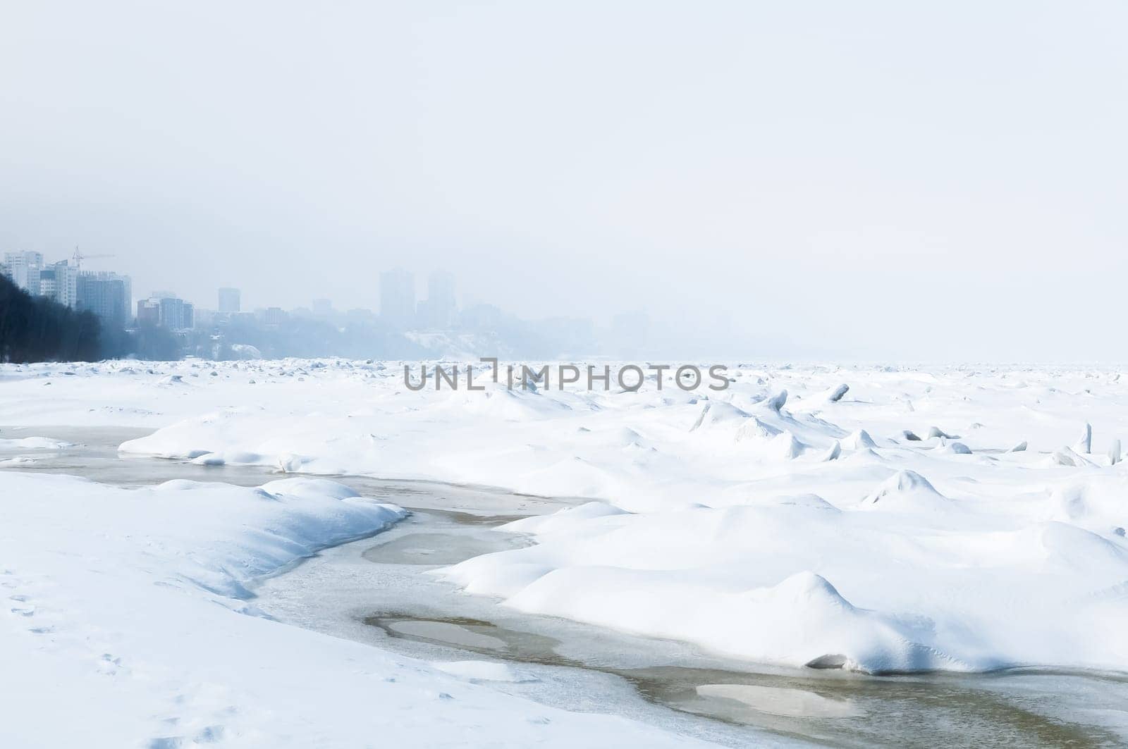 Stunning view of the frozen river covered with chunks of ice and white frosted snow. Snowy desert. The river breaks through the ice.