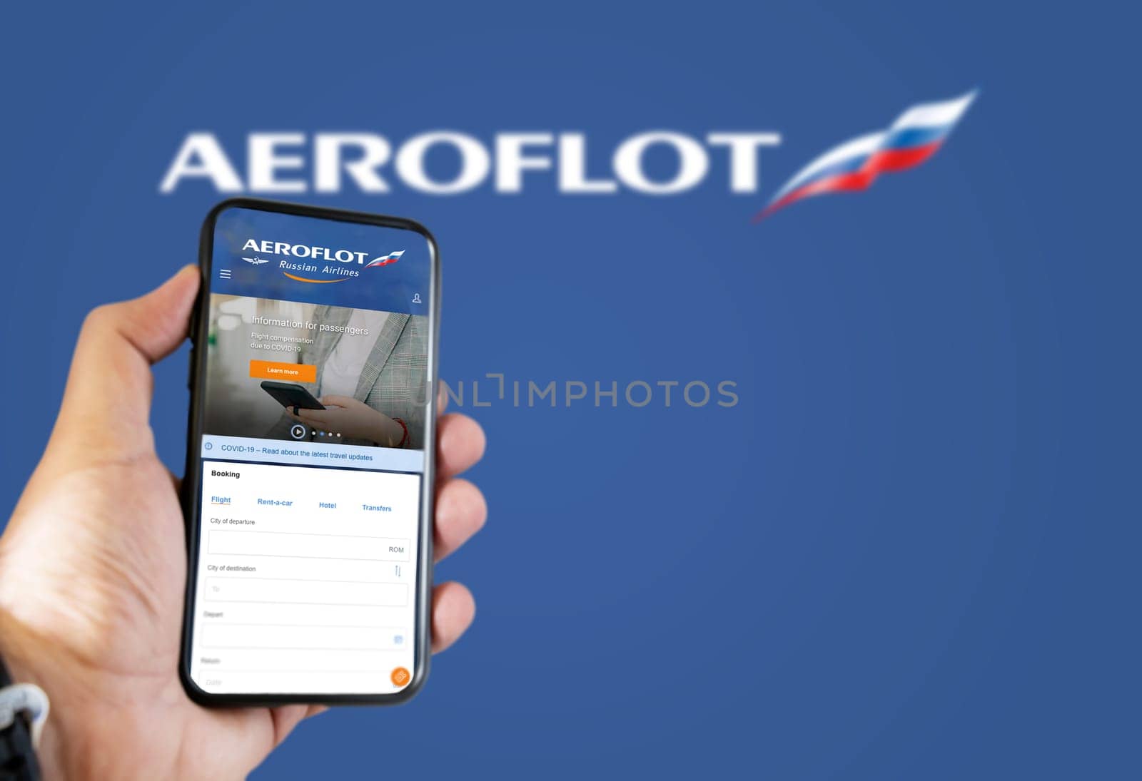 Moscow, January 2022: Hand holding a phone with Aeroflot russian airlines flight booking application. Aeroflot logo blurred on a blue background. Booking airline tickets