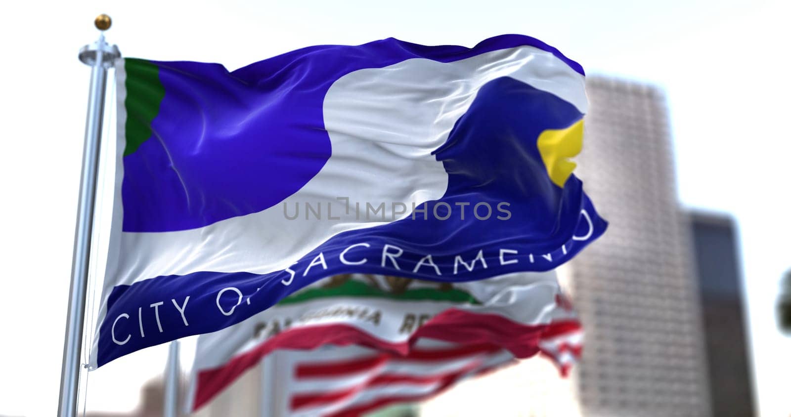 Sacramento city flag waving in the wind with California state and United States national flags blurred in background. Sacramento municipal flag