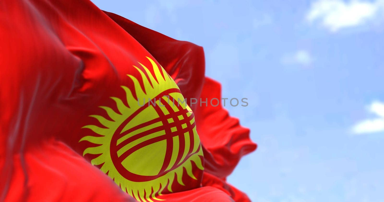 Detail of the national flag of Kyrgyzstan waving in the wind on a clear day. Kyrgyzstan is a mountainous landlocked country in Central Asia. Selective focus.