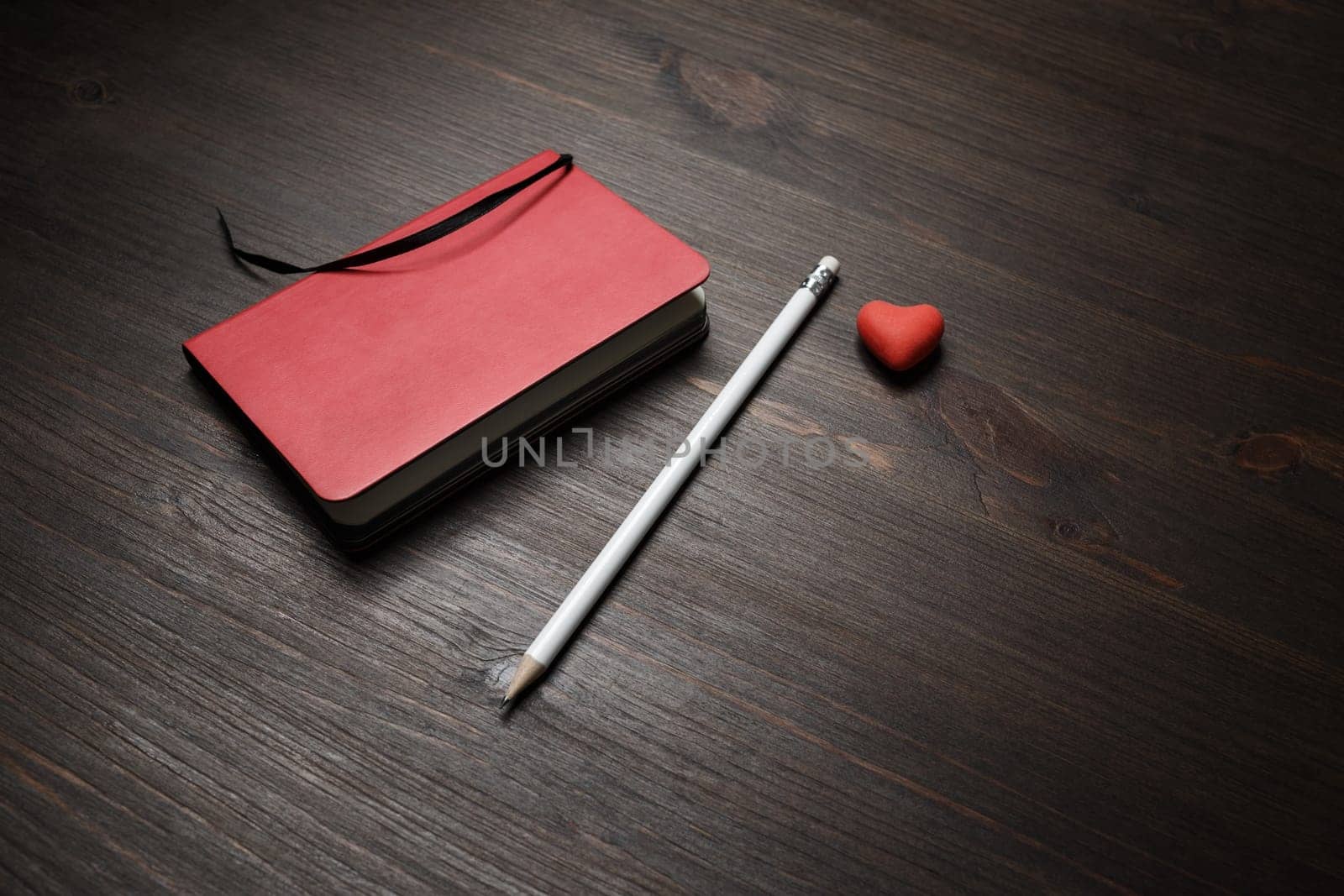 Photo of blank red notebook, pencil and heart-shaped eraser on wooden background.
