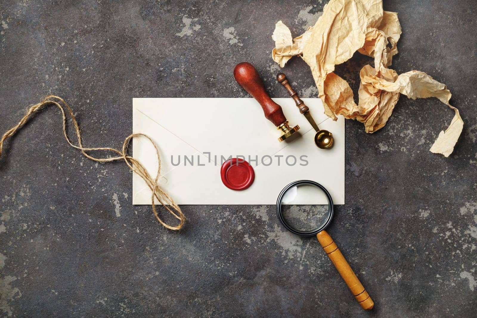 Vintage postal stationery on concrete background. Blank envelope, sealing wax, stamp, spoon, magnifier, crumpled paper and rope.