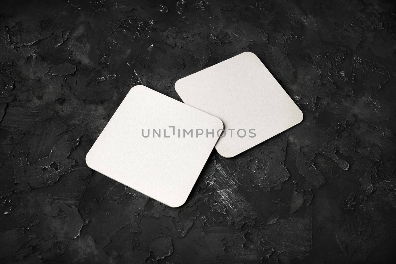 Two blank square beer coasters on black plaster background. Responsive design template.