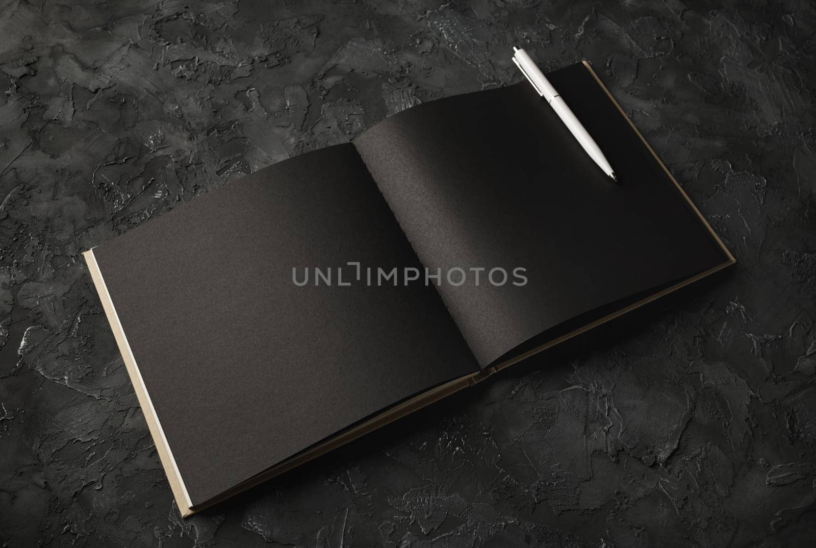 Blank black paper sketchbook and pen on black plaster background. Responsive design template.