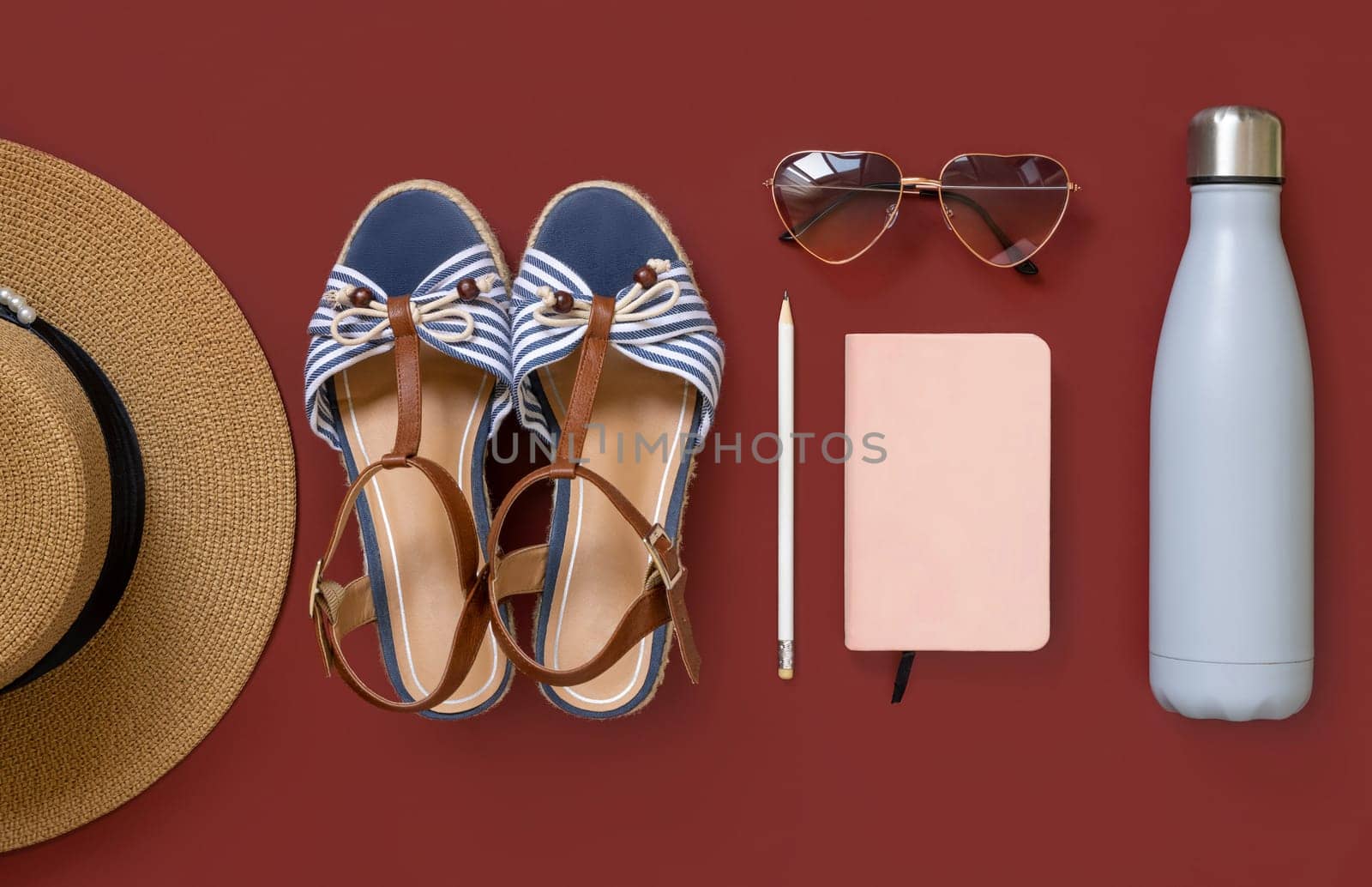 Straw hat, denim shoe, notebook, heart sunglasses and reusable bottle top view on red background. Female summer clothes and accessories flat lay. Hardcover textbook and bottle mockup. Travel concept